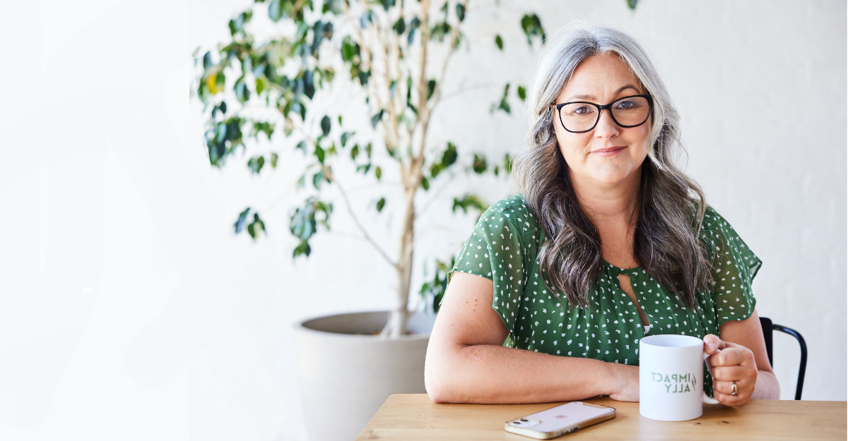 picture of woman (laura swindley) sitting at desk in green dress and white glasses