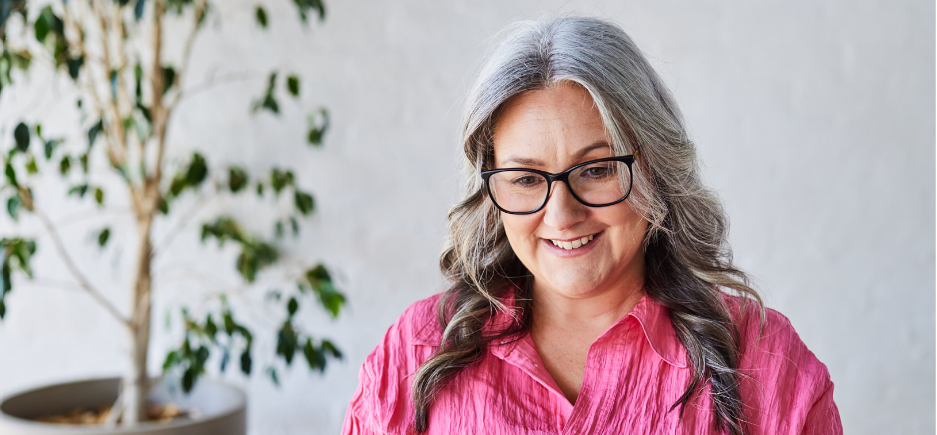 woman with glasses in pink shirt looking down at computer and smiling